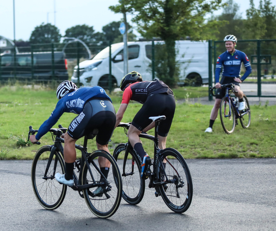 A rider and a coach sprint to the line on road bikes.